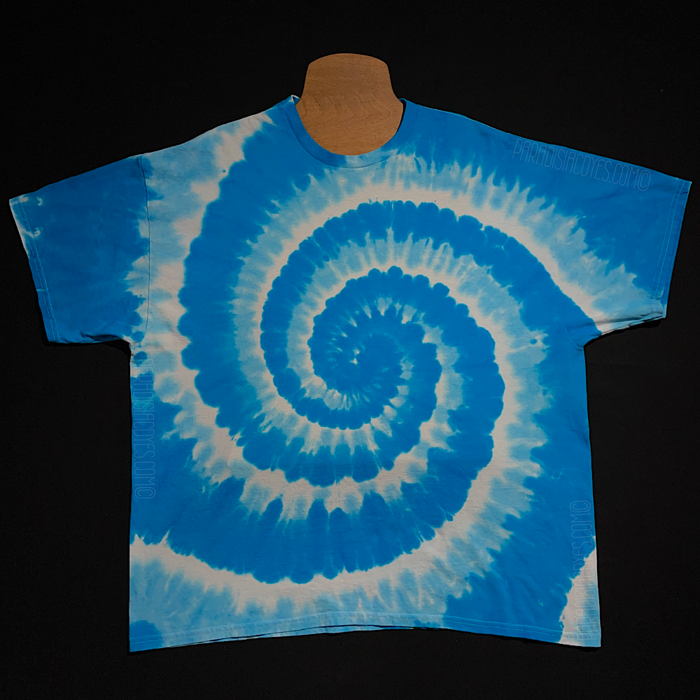 Front side of an aqua & electric blue, with white, spiral tie dye t-shirt design; laid flat on a solid black background 