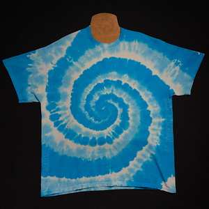 Front side of a bright aqua blue & white spiral tie dye design short sleeve shirt; laid flat on a solid black background