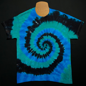 A black, blue & teal spiral tie dye short sleeve shirt laid flat on a solid black background.