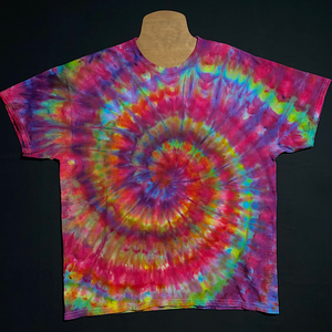 An example of a finished, one-of-a-kind Confetti Rainbow Ice Dye Spiral T-Shirt design; laid flat on a solid black background