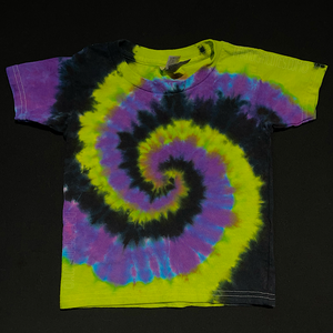 A toddler sized black, green & purple spiral tie dye short sleeve shirt; laid flat on a solid black background.