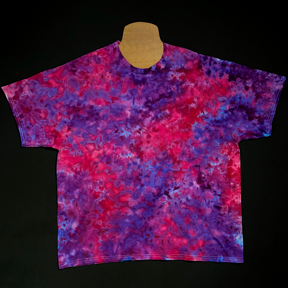 An example of a pink & purple ice dyed splatter pattern short sleeve t-shirt; laid flat on a solid black background