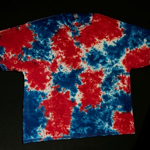 An example of another finished red, white & blue splatter pattern tie dye t-shirt; laid flat on a solid black background