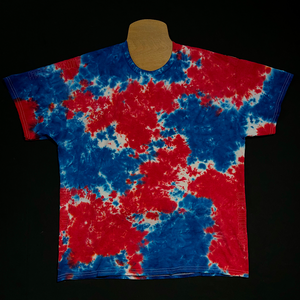 A hand-dyed, one-of-a-kind red, white & blue splatter pattern short sleeve tie dye shirt; laid flat on a solid black background.