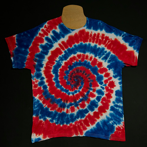 Red, white and blue American flag colored short sleeve spiral tie dye t-shirt; laid flat on a solid black background.