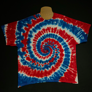 Example of a different Fourth of July red, white & blue spiral tie dye short sleeve shirt; laid flat on a solid black background.