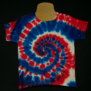 A toddler sized short sleeve shirt featuring a red, white & blue spiral tie dye design.