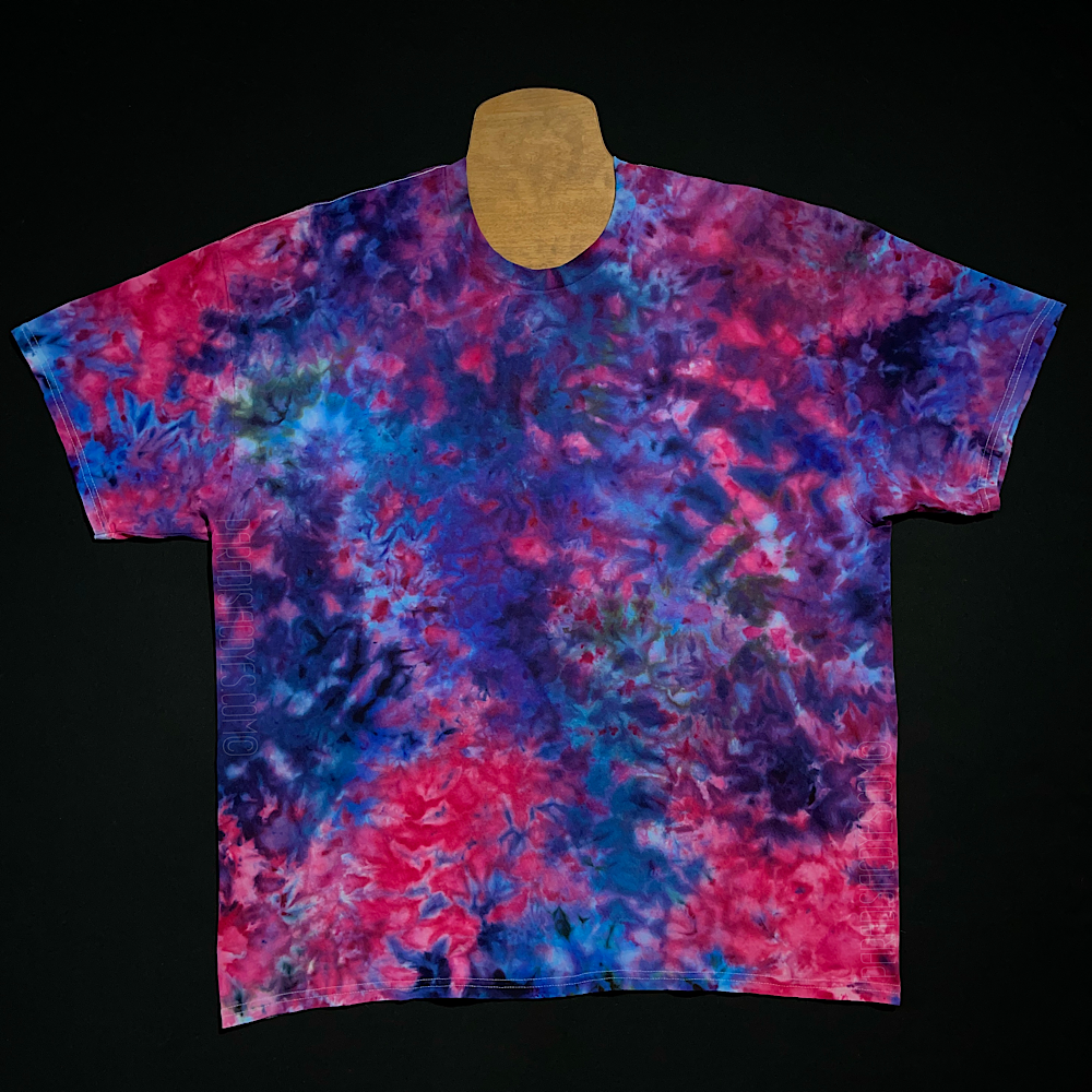 Front side of a finished, one-of-a-kind blue, pink & purple marbled ice tie-dyed short sleeve shirt design; laid flat on a solid black background before shipping