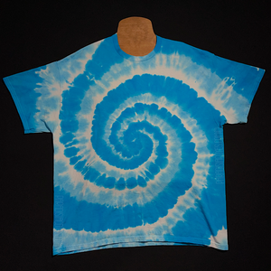 Front side of a bright aqua blue & white spiral tie dye design short sleeve shirt; laid flat on a solid black background 