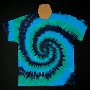 An example of a different, finished black, blue & teal spiral tie dye t-shirt before shipping; laid flat on a solid black background