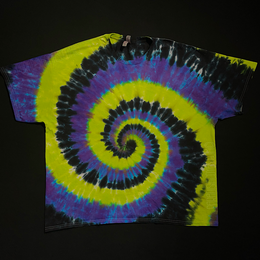 A black, green & purple spiral tie dye tee; laid flat on a solid black background.