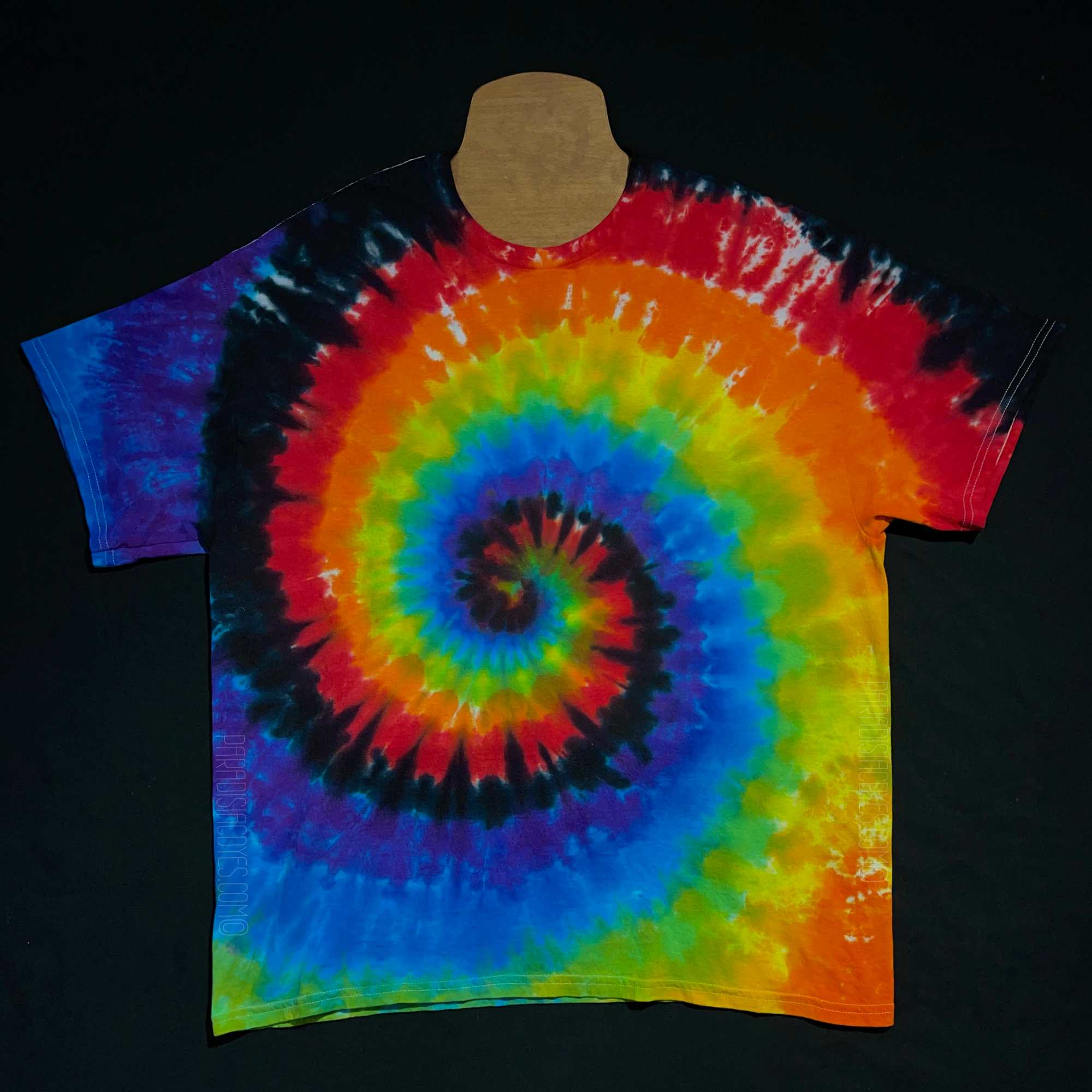 An example of a finished, one-of-a-kind, hand-dyed when ordered rainbow tie dye t-shirt, featuring: red, orange, yellow, green, blue, purple & black in a spiral design