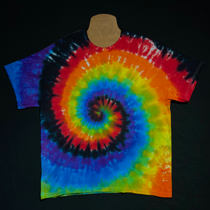 An actual, finished Black Rainbow Spiral Tie Dye T-Shirt; laid flat on a solid black background before shipping, to demonstrate how much each made-to-order tie dye shirt may vary despite being made in the same colors & pattern
