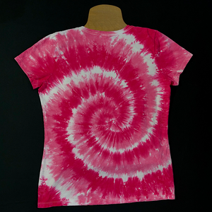 Back side of a ladies' v-neck style short sleeve tie dye t-shirt featuring a bright bubblegum pink & white spiral design; laid flat on a solid black background 