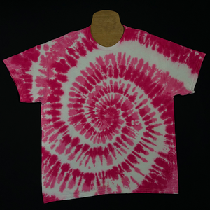An example of a finished, one-of-a-kind, bubblegum pink spiral tie dye t-shirt design before shipping; laid flat on a solid black background