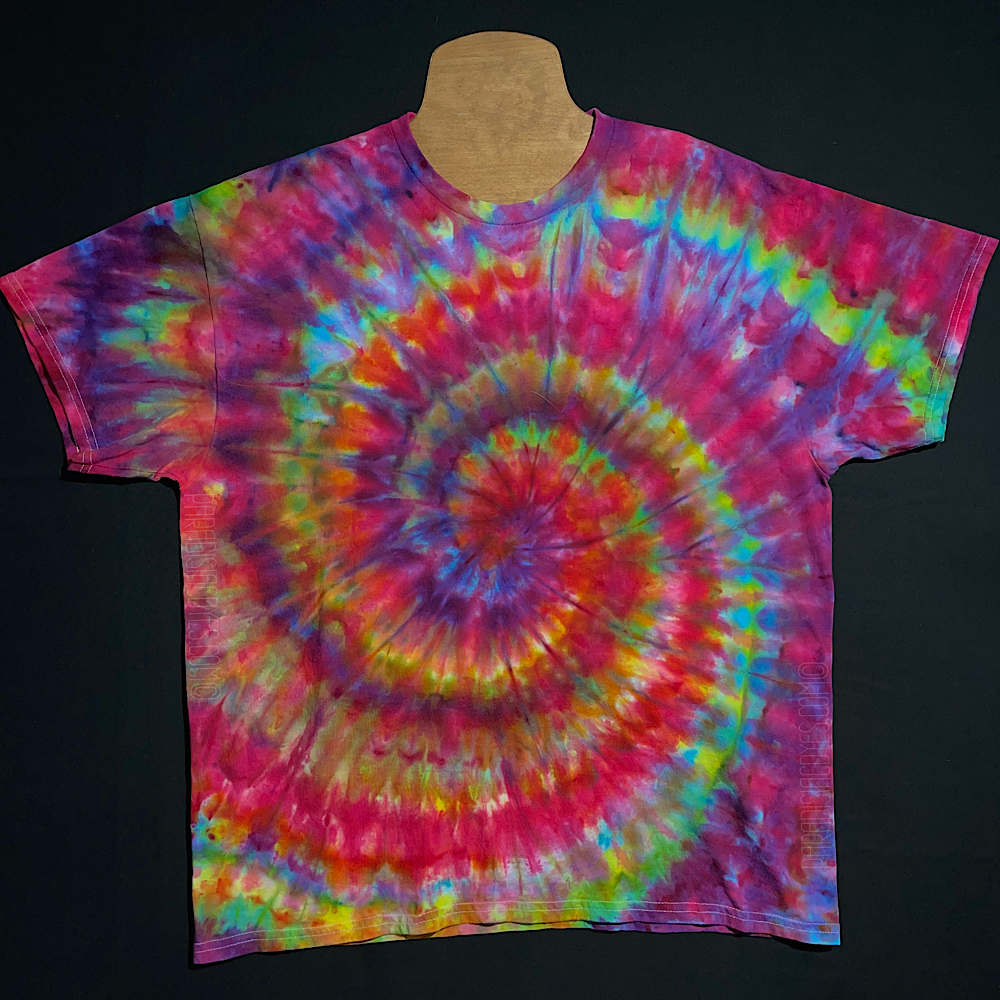 An example of a finished, one-of-a-kind Confetti Rainbow Ice Dye Spiral T-Shirt design; laid flat on a solid black background 