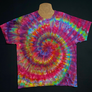 An example of a finished, one-of-a-kind Confetti Rainbow Ice Dye Spiral T-Shirt design; laid flat on a solid black background 