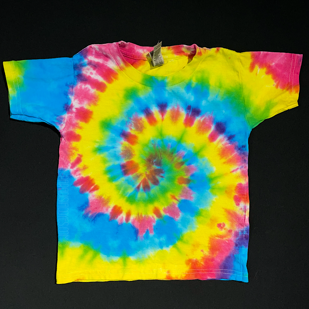 A toddler sized short sleeve t-shirt featuring a hot pink, fluorescent yellow & electric blue tie-dyed spiral design; laid flat on a solid black background.
