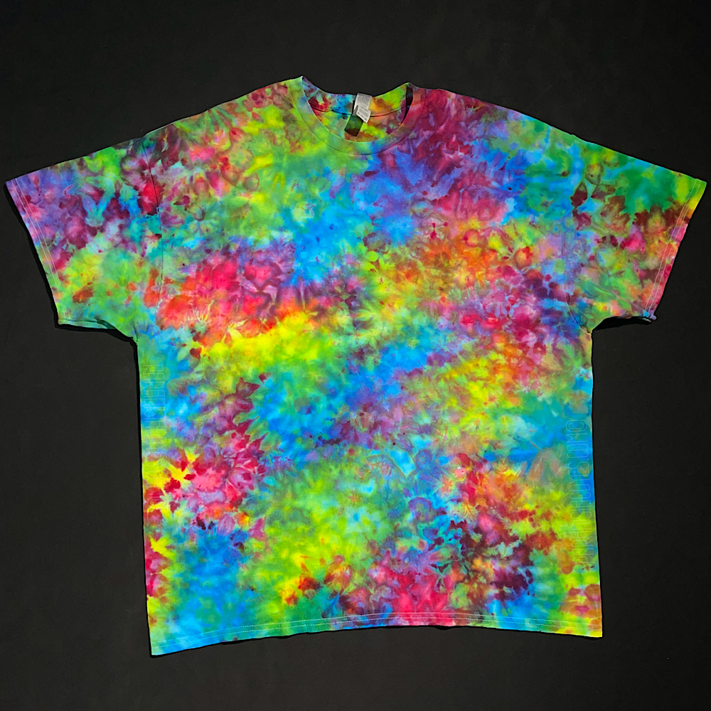 A marbled splatter pattern ice tie-dyed t-shirt design featuring a superman ice cream inspired blend of blue, pink & yellow shades; laid flat on a solid black background
