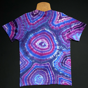 Back side of an agate geode inspired tie dye t-shirt featuring a multitude of purple shades, laid flat on a solid black background