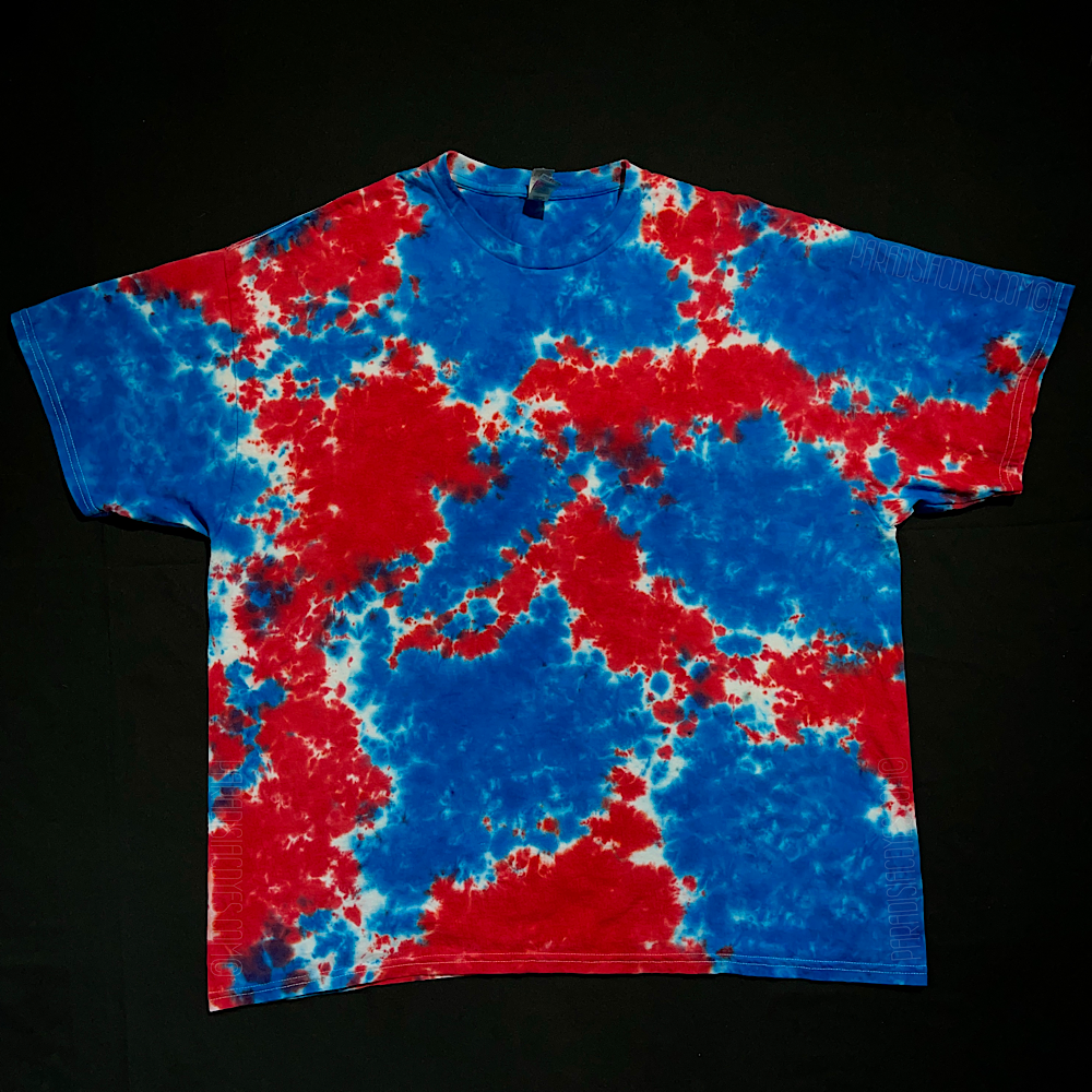 An example of a finished, hand-dyed, one-of-a-kind red, white & blue splatter pattern short sleeve tie dye t-shirt; laid flat on a solid black background 