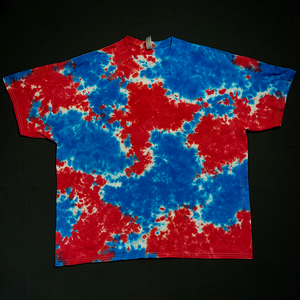 Front side of a red, white & blue splatter pattern tie dye short sleeve shirt; laid flat on a solid black background