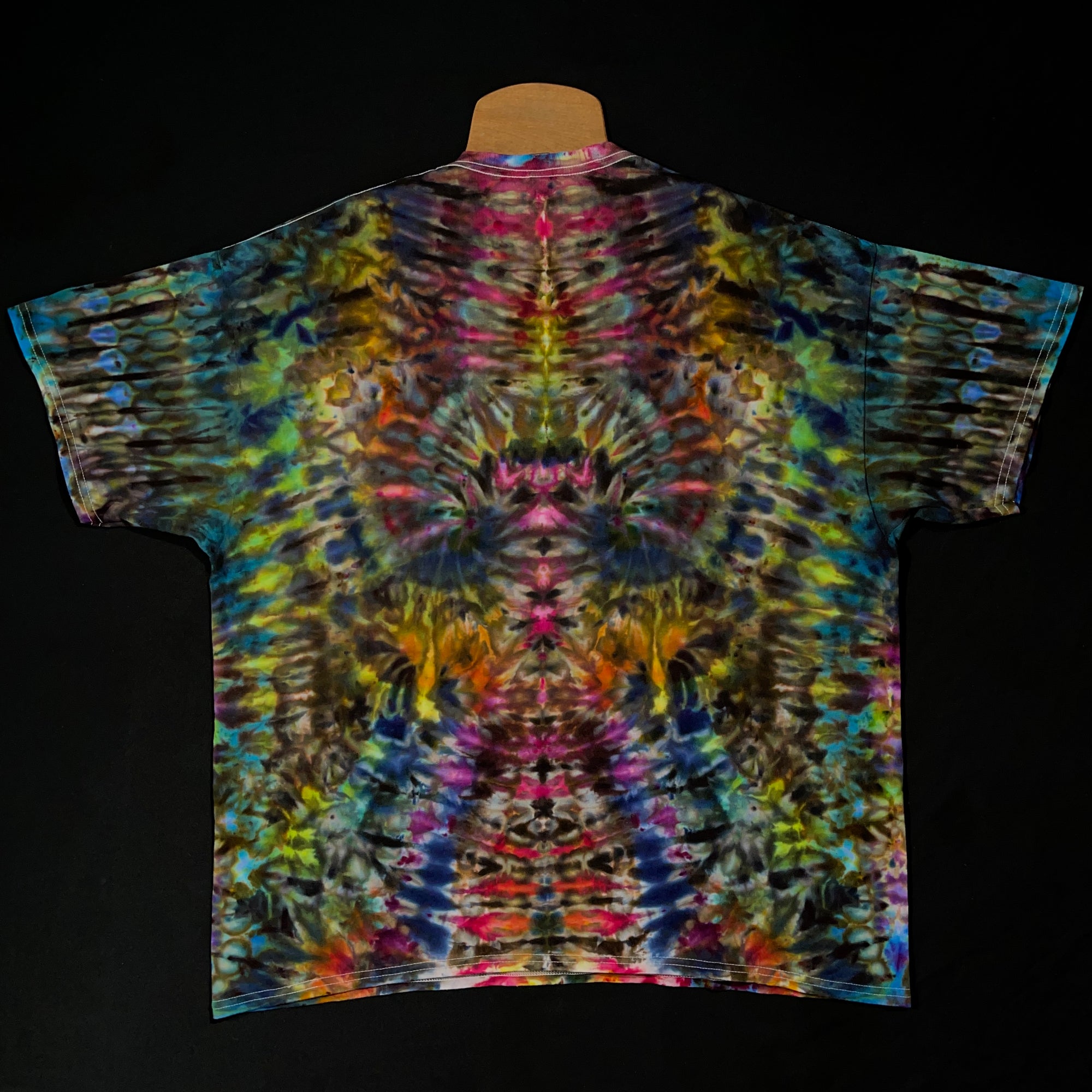 Back side of the same abstract, symmetrical rainbow ice tie-dyed t-shirt design; laid flat on a solid black background 