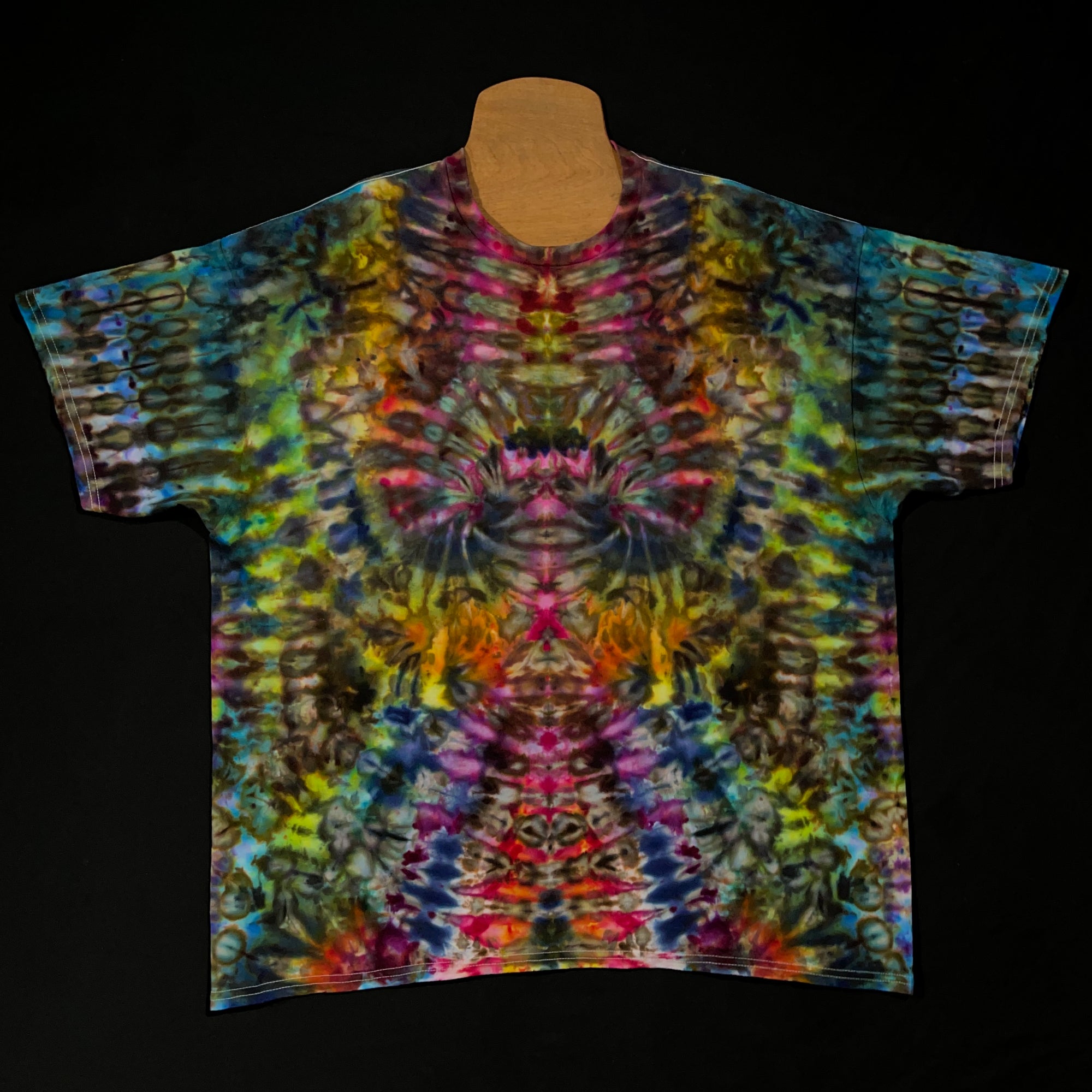 Front side of a size xxl rainbow colored abstract, symmetrical ice tie-dyed short sleeve shirt design; laid flat on a solid black background 