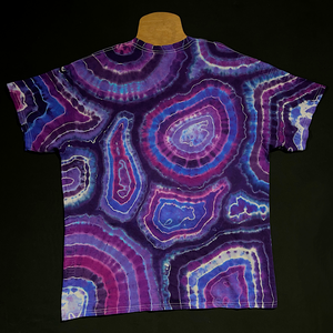 Back side of an Amethyst Quartz geode pattern short sleeve tie dye shirt featuring an array of purple shades with a distinctly different pattern on each side; laid flat on a solid black background 