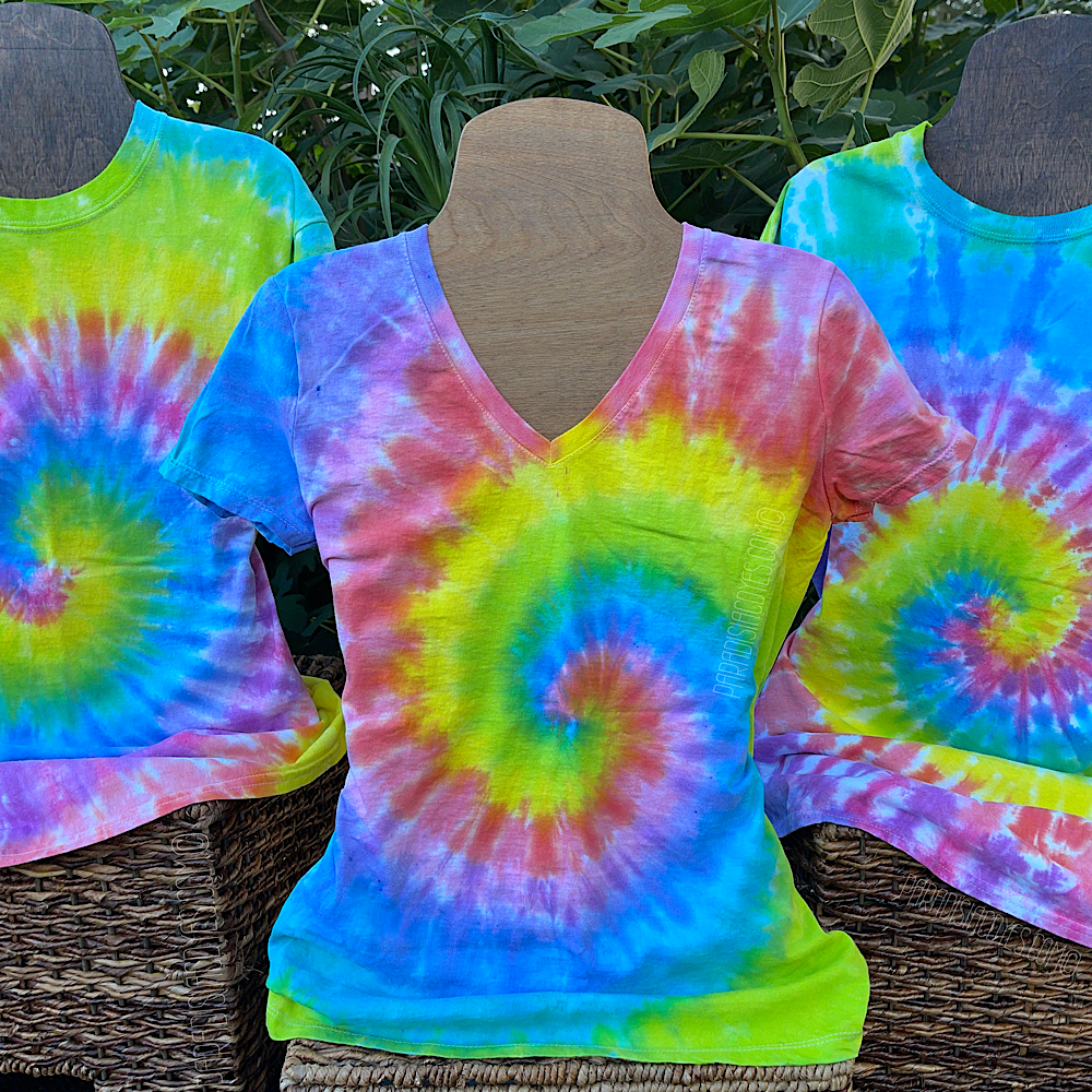 Three pastel rainbow spiral tees displayed on t-shirt mannequins in natural sunlight