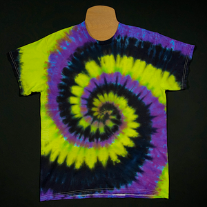 The front side of a black, neon lime green and purple with blue edges spiral tie dye t-shirt, displayed on a mannequin, lying flat on a solid black background