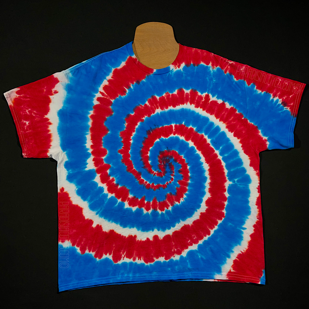 Another example of a hand-dyed, one of a kind red, white and blue Fourth of July spiral tie dye shirt design, lying flat on a solid black background