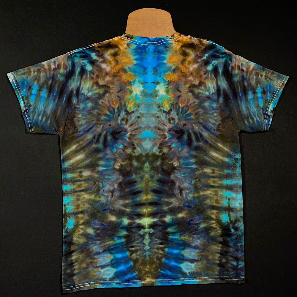 Front side of a short sleeve size adult medium tie dye shirt featuring an abstract, symmetrical, totem pole like ice dyed pattern in an array of blue, brown & golden shades 