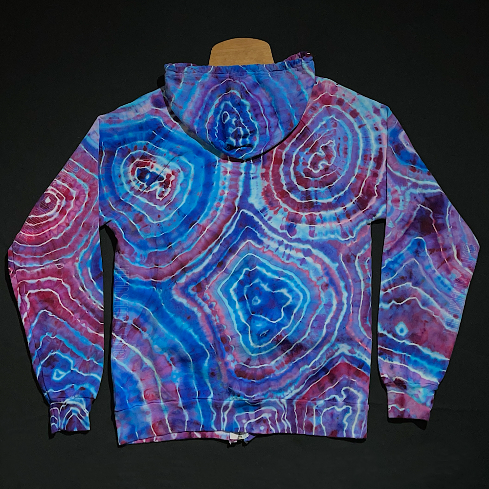 Back side of a size medium zip up tie dye hoodie featuring a pink & blue cotton candy color scheme in an ice dyed agate geode design, laid flat on a solid black background 