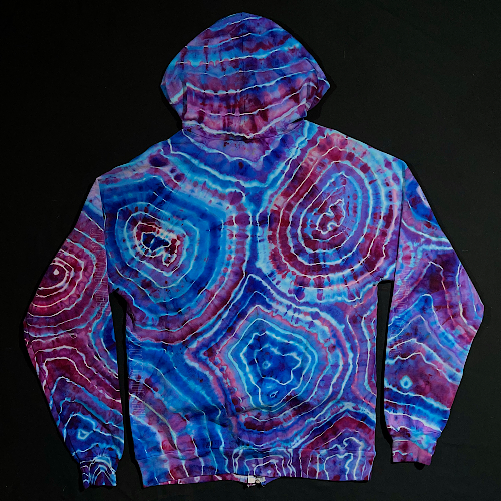 Back side of a size medium zip up style ice tie dye hoodie featuring a pink & blue cotton candy geode design with a totally different pattern on each side, laid flat on a solid black background 
