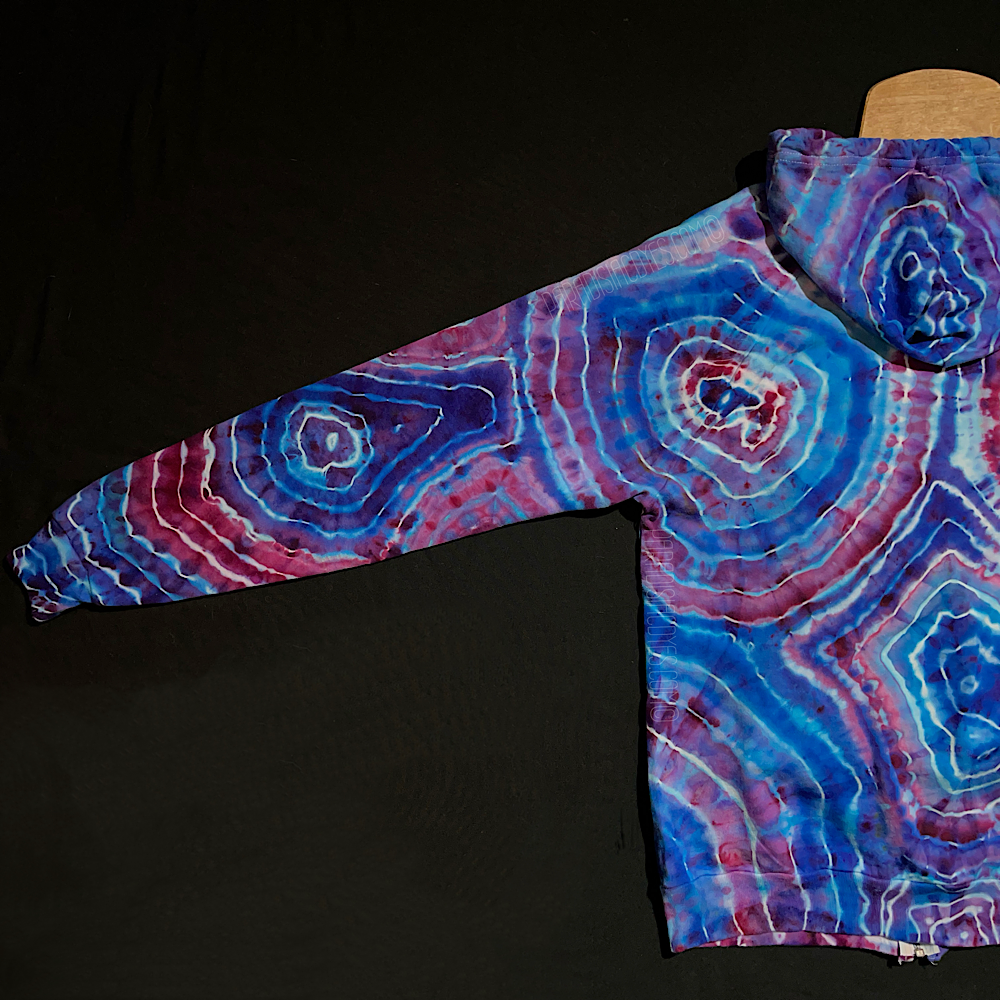 The back side of the front left arm sleeve on a size adult medium cotton candy agate geode ice tie dyed zip up hoodie; fully extended laid flat on a solid black background 