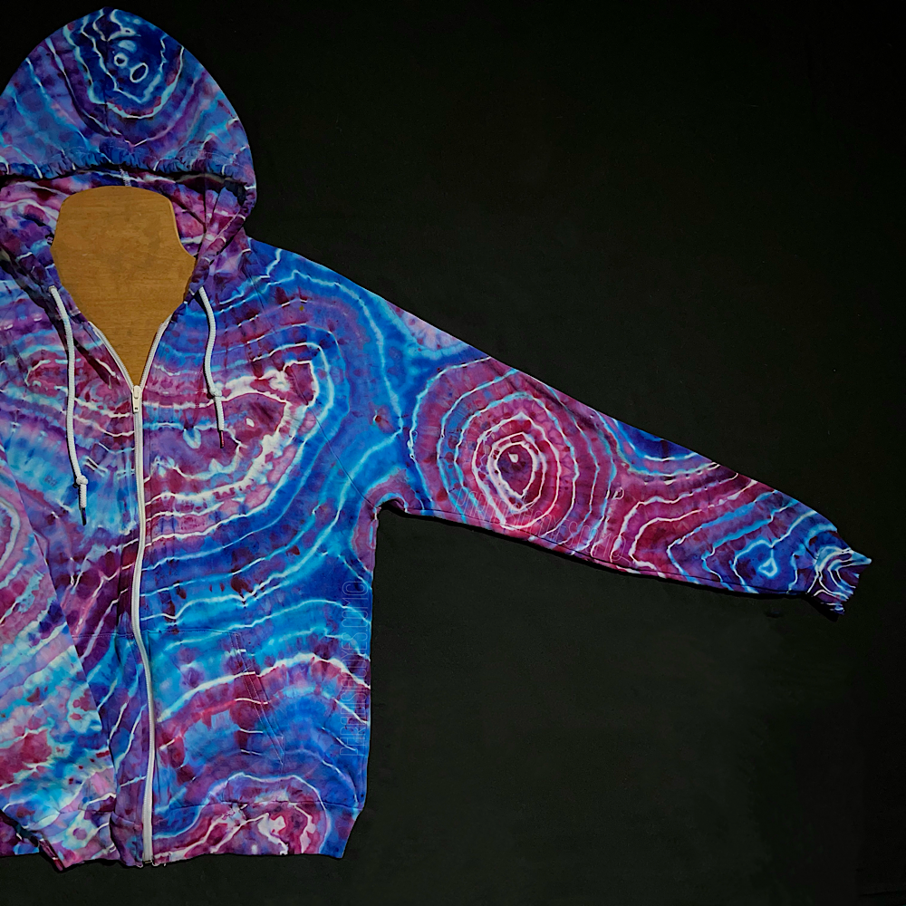Front left side sleeve of a cotton candy agate geode ice dye zip up hoodie; fully extended laid flat on a solid black background 